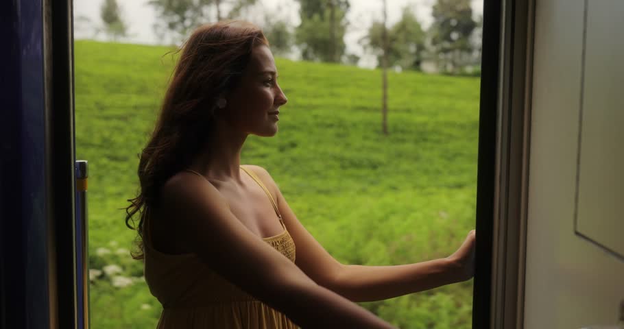 Travel and exploration of tourist woman by Sri Lankan train in second class wagon to famous places of the country. Romantic young traveler woman enjoying extreme train ride, looking out to the door on