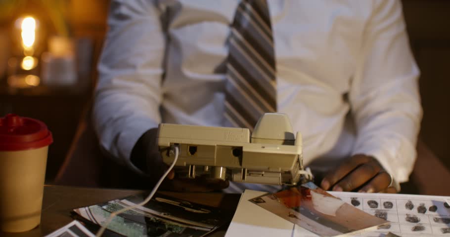 A business man is talking on the phone with a serious look. He's sitting at the table. Detective agency.
