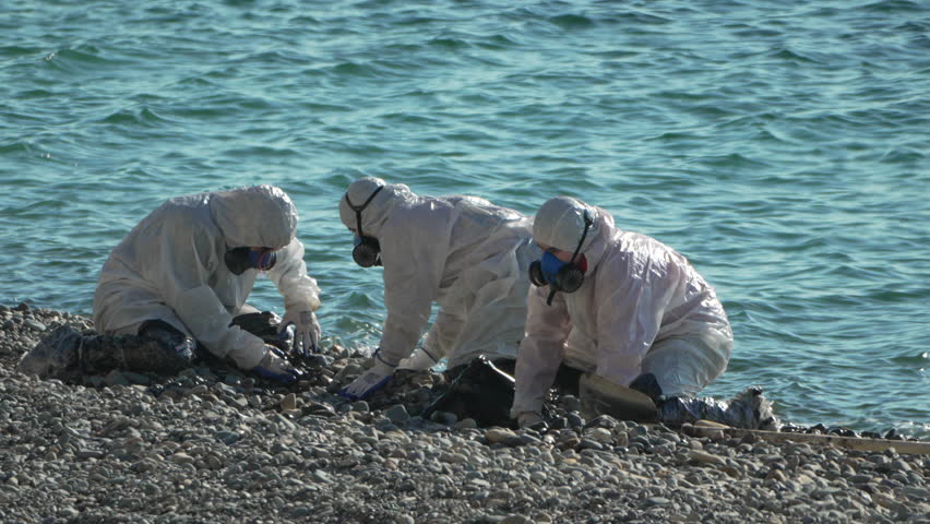 Hazmat Team Coastal Cleanup Pollution Investigation: Workers in protective suits collect samples near ocean, likely due to environmental contamination.