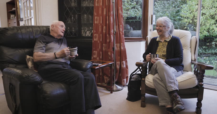 Coffee, talking and love with a senior couple sitting in the living room of their retirement home together. Tea, conversation or bonding with a mature man and woman chatting in the lounge of a house