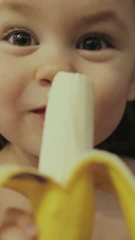Adorable and Cute Toddler Joyfully Enjoying a Delicious Banana Snack on a Sunny Day. Vertical video.