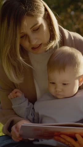 Vertical Screen: Young mother enjoys quality time with her baby, reading a book together in a peaceful park setting