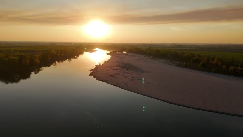 Golden sunset light casts warm reflection on the Adda and Po rivers confluence near Isola Serafini, near Maginot in Olza di Castelvetro, revealing a sandy bar edging calm riverbanks under pastel sky