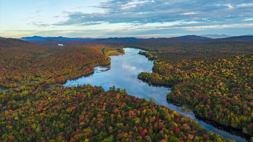 Sunlight Shifting Across Autumn Forest Surrounding Lake In Adirondack Mountains. aerial shot, timelapse