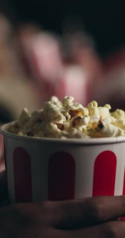 Person, hands and popcorn with movie in cinema at night for entertainment, show or film. Closeup, consumer or customer with food or snack in dark theater for suspense, eating or watching at center