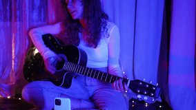 Young woman musician illuminating bedroom with pink and blue lights while playing acoustic guitar and singing, capturing intimate musical moment with genuine emotion and creativity - Powered by Shutterstock - Get 15% off with code: PIKWIZARD15