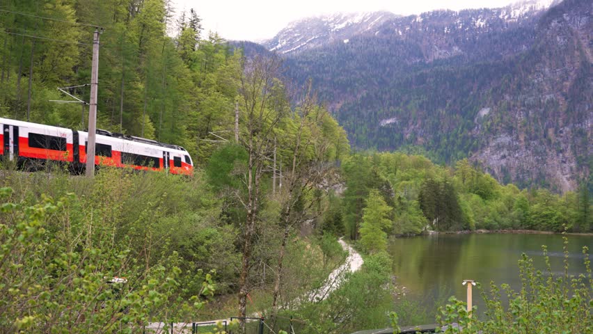 Red train in Austria. The train moves along the green trees and  lake. Red  train in  in Austrian alps mountains.. Red train in Hallstatt, Austria.