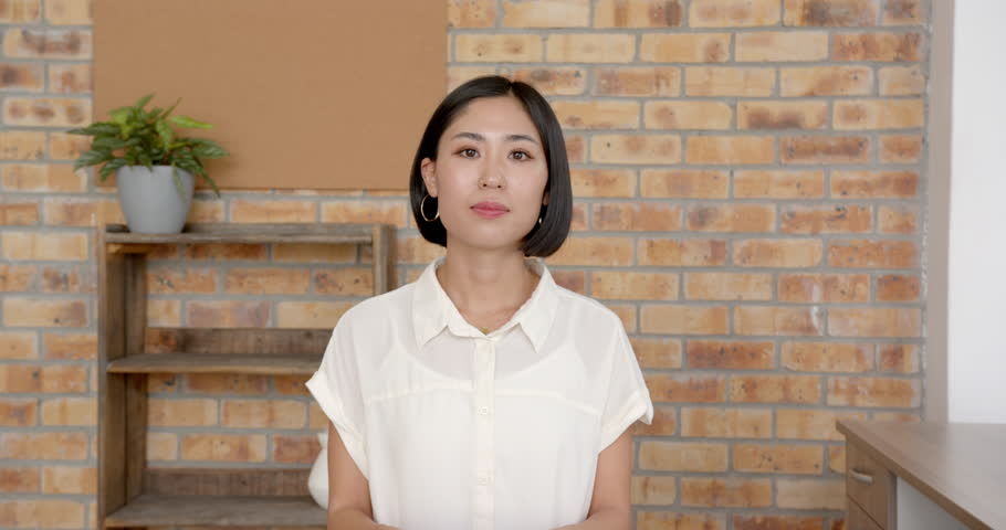 Close up of people talking to the camera, smiling woman standing in office, wearing white blouse, looking at camera. the person is fully visible, sitting, half body