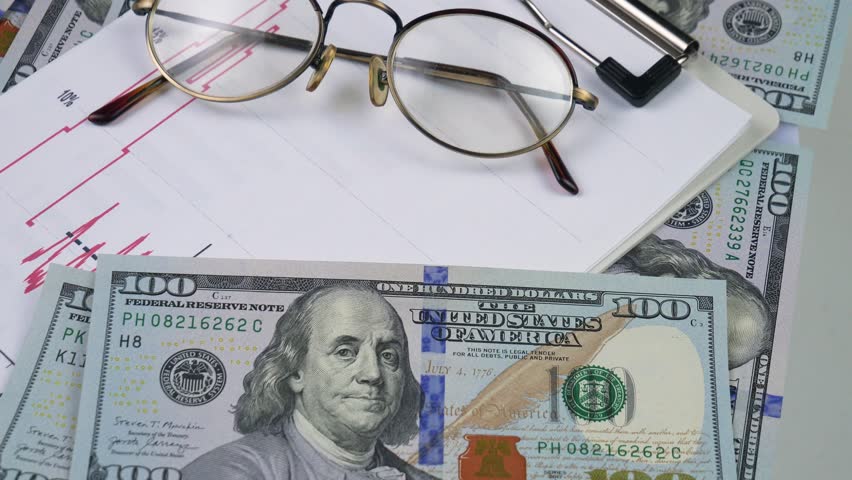 Dollar bills falling on business papers. Close-up. Slow motion.