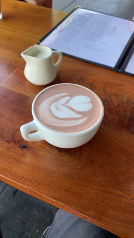 Coffee cup with leaf drawing in a restaurant or cafe shop. POV from phone or food critic content creator influencer filming table. UGC vlog style. Tasty drink in hip place. User generated content