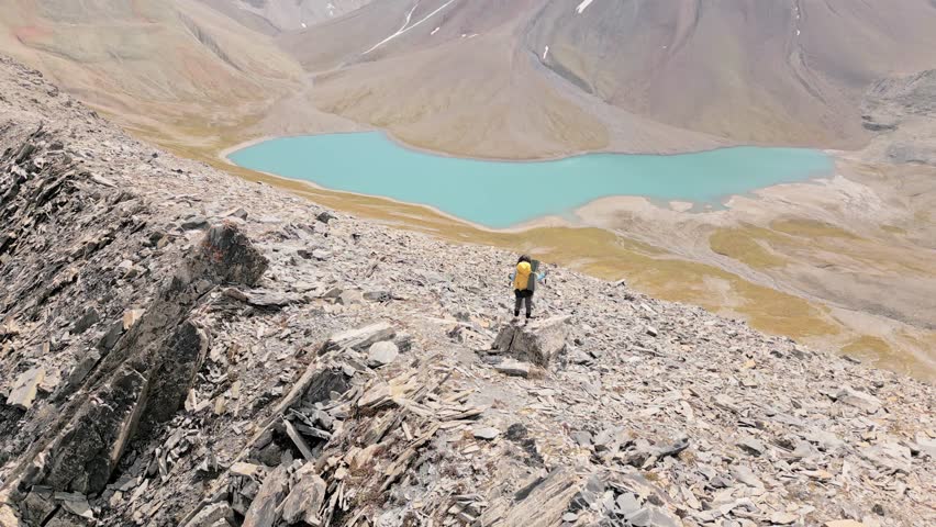 Aerial rising view young woman Hiker standing and watching beautiful alpine lake and mountains in country Georgia. Kazbegi, Kelitsadi lake, Georgia