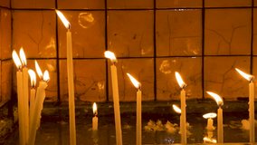 Many Candles flicker in dimly lit, warm glow against textured tiles. Melted wax drips. Calm and reflection. Spirituality, tranquility, warmth. People light candle in dark church for repose of soul. - Powered by Shutterstock - Get 15% off with code: PIKWIZARD15