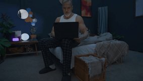 Senior grey-haired man in pajamas working on laptop in dark bedroom, then going to sleep during late night - Powered by Shutterstock - Get 15% off with code: PIKWIZARD15