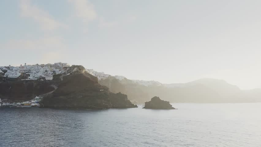 Santorini island, Greece. White architecture on the cliffs. View from the sea at foggy sunrise. Blue sea and the blue sky. Travel and summer vacation. 
