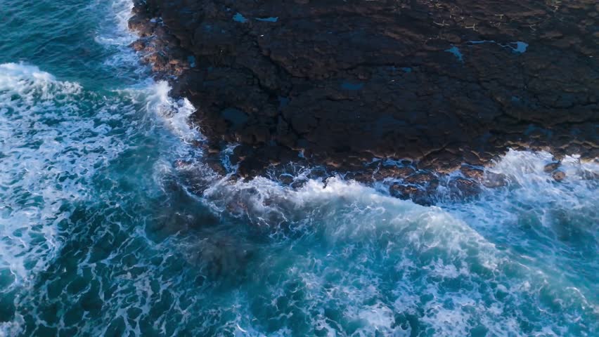 Aerial top-down view of ocean waves crashing onto rocky shorelines in Mauritius, showcasing raw coastal beauty and dynamic sea motion.