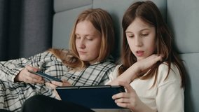 Two teenage girls lie side by side, fully absorbed in their smartphone and tablet screens in a calm indoor setting. High quality 4k footage - Powered by Shutterstock - Get 15% off with code: PIKWIZARD15
