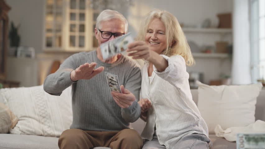 Positive elderly married couple enjoying richness and happiness, throwing money. Portrait of happy mature husband and wife in living room, successful big deal or win in lottery, aged people and cash