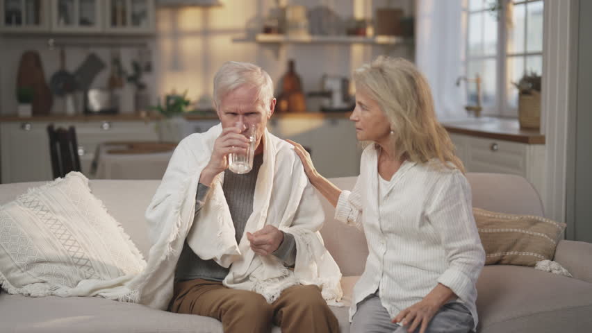 Curing influenza or heart attack by pills, old man taking tablet, feel bad. Portrait of elderly woman and her husband in home interior, modern medicine and healthcare, disease, illness of aged people