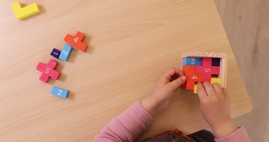 close-up of little child girl collects 3d puzzle on table, top view