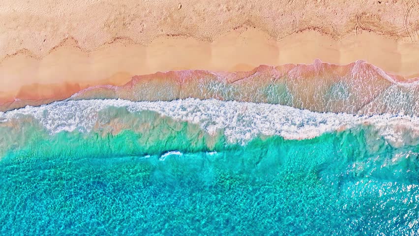 Turquoise sea waves with white foam on yellow sand, drone view. Tropical sea beach background. Calm wave with sunlight reflection. Ocean beach at high tide.