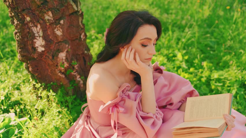 happy woman beauty princess sitting under tree reading paper book. Summer garden park green grass spring nature magic sun light, Lady holding novel art. long pink dress old style. sexy girl model 4k