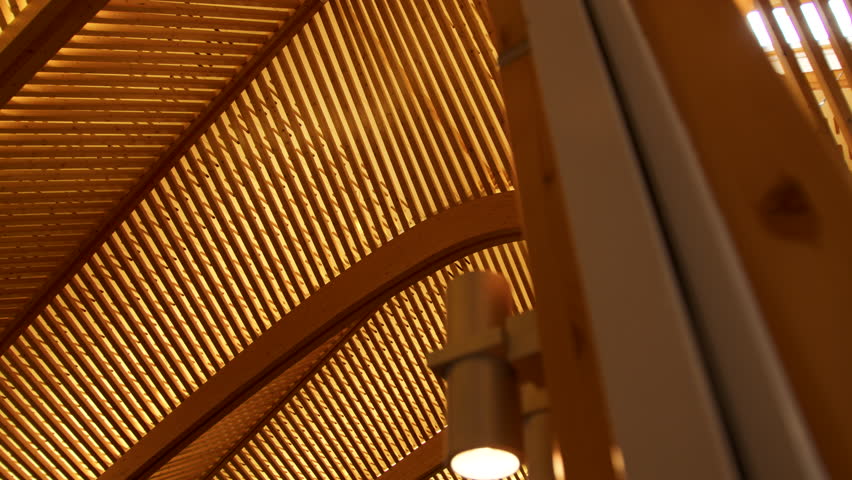 Medium lateral tracking shot of the wooden framework, with a foreground post reinforcing the sense of motion. The wood architecture is emphasized.
