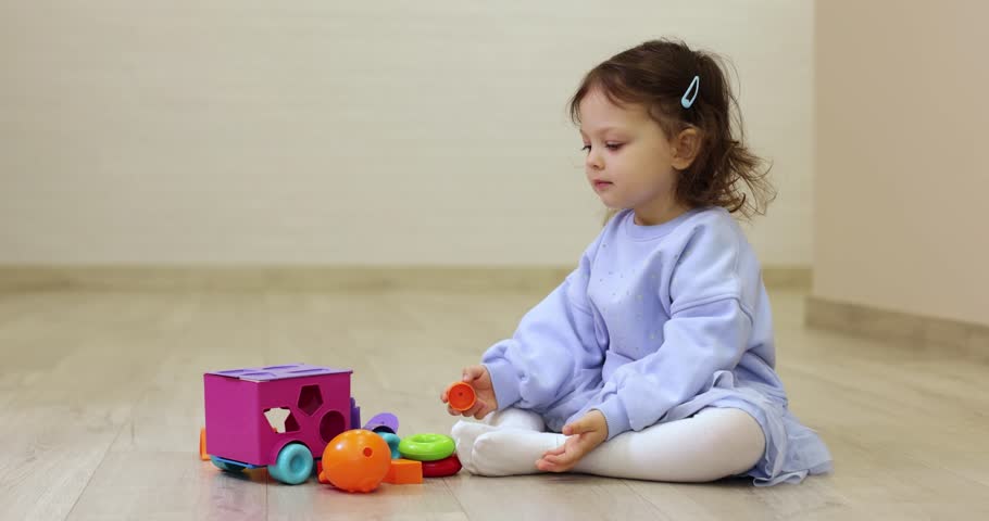 toddler child girl playing with shape sorter toy on floor, educational playtime at home. Cognitive development activity