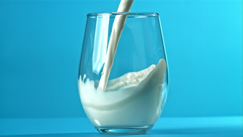Fresh milk is poured into a glass on a blue background. Filmed on a high-speed camera at 1000 fps. High quality FullHD footage