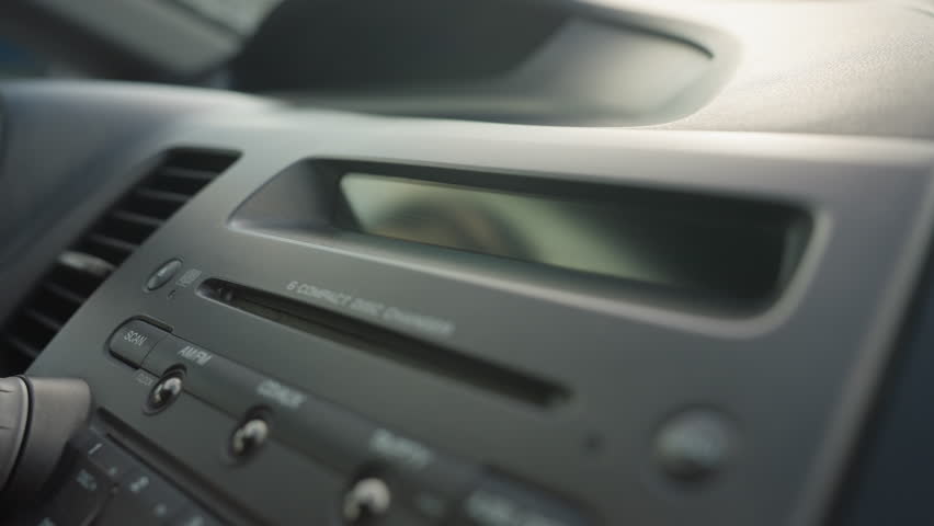 close up of dashboard showing stereo control panel and cd display screen blinking inside parked car under daylight with visible air vent and buttons around media console