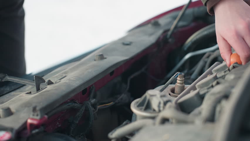 Close up of exposed car engine with red dipstick pulled out for oil level check during winter vehicle maintenance, snowy background visible