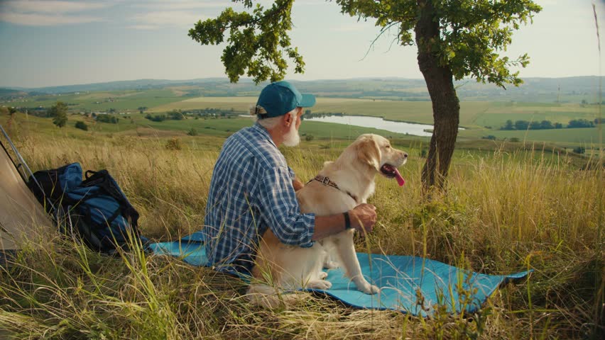 Digital Detox, Nature Healing. Senior Man Sits With His Dog by a Tent, Admiring the Mountain View. A Quiet Moment of Disconnection, Mental Recharging, and Deep Presence in Nature