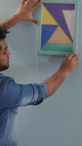 African-America men hang abstract drawing straight on wall in studio backside view. Art object for interior design trends. Work upon domestic style