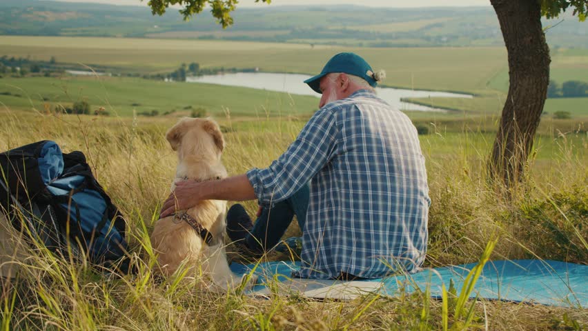 Human-Animal Bond in Nature. Senior Man Sits Beside His Dog Near a Tent, Watching the Majestic Mountains. A Deep Moment of Connection, Trust, and Companionship Surrounded by Wilderness