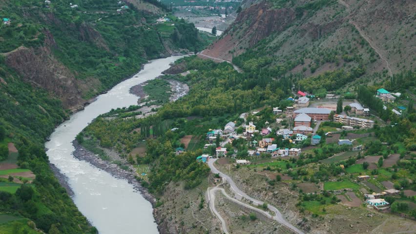4K Aerial shot of beautiful small village near Chenab river flowing in Lahaul, Himachal Pradesh, India. River flowing in mountain valley. Summer in Himalayas.