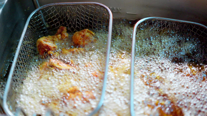 Close-up of crispy fried chicken pieces sizzling in hot oil inside a deep fryer in a Restaurant, showcasing delicious cooking in a kitchen.