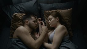 Top view of young man and woman in underwear lying in bed at home, facing each other, enjoying bond and connection. Gentle touches, subtle smiles, soft look in eyes, love in air, copy space - Powered by Shutterstock - Get 15% off with code: PIKWIZARD15