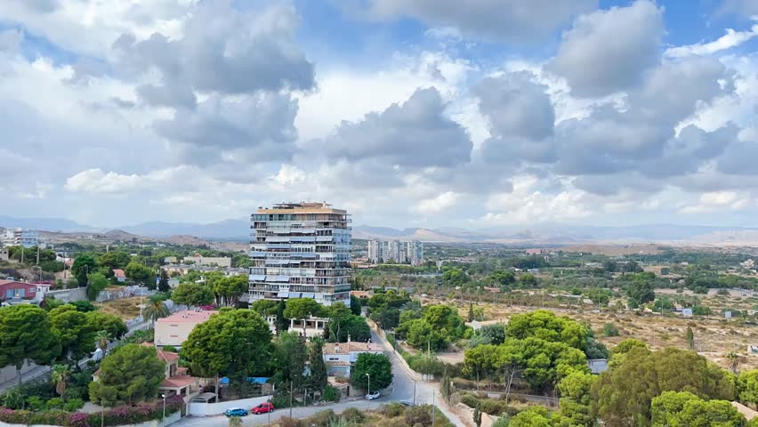 Timelapse footage showing a panoramic view from a balcony above Alicante, Spain. Clouds drift over the mountains and city rooftops, capturing the dynamic beauty of the urban and natural landscape.