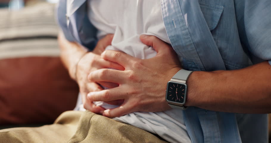 Hands, tummy ache and man on sofa in home for indigestion, diarrhea or food poisoning. Illness, sick and male person with stomach pain for constipation, IBS or abdominal muscle strain in house.