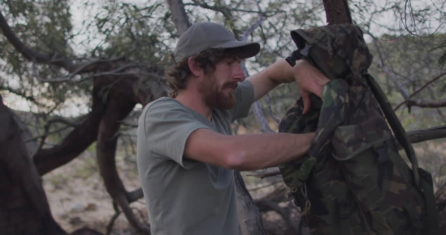 Man adjusting camouflage backpack outdoors, showcasing floating social media notifications and bars. Adventure, exploration, rugged, urban, modern, technology, resilience