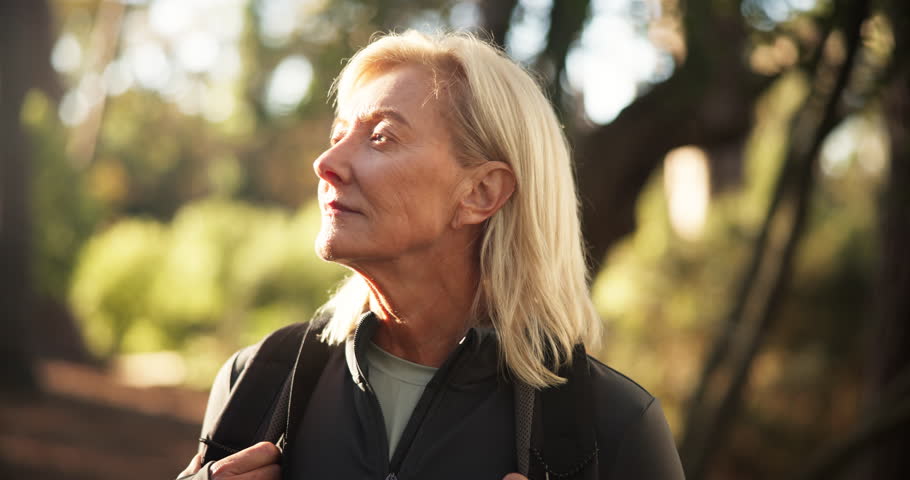 Hiking, mature woman and face in woods for adventure, retirement hobby and cardio wellness. Senior person, smile and portrait with backpack for trekking, explore and holiday sightseeing in forest