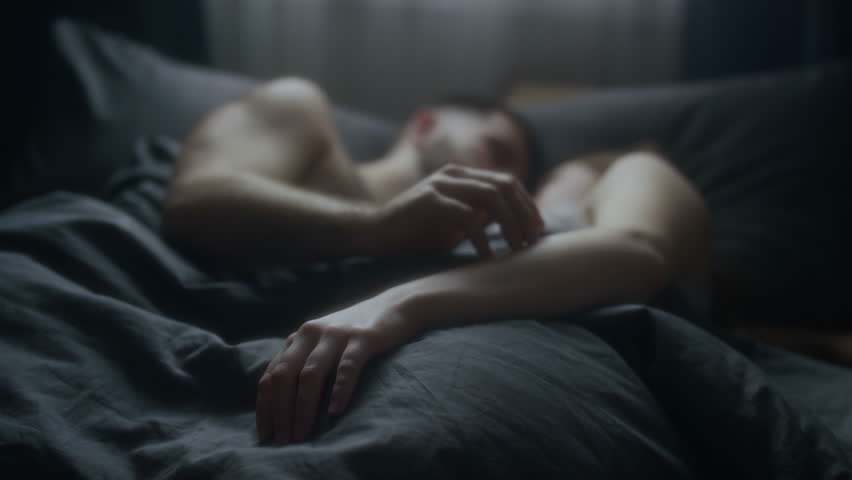 Close-up of young spouses intertwining fingers and holding hands while peacefully snuggling in bed after sleep in morning, deep love, affection and intimacy, focus of hands