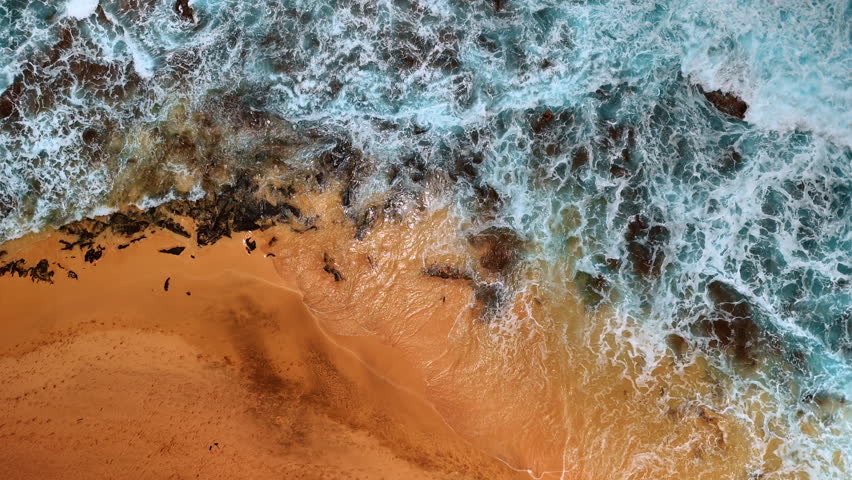 White foamy waves splash on the sandy beach and rocks sticking out of shore. Beautiful Pacific Ocean at the coast. Top view.