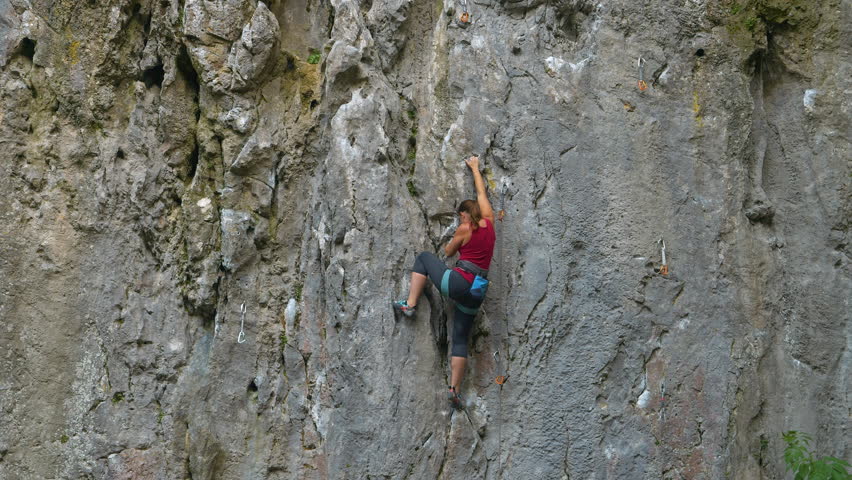 Cool shot of an athletic young woman top rope climbing a steep wall in the tranquil summer nature. Sporty Caucasian woman rock climbing a steep, textured limestone wall outdoors. Extreme rock climbing