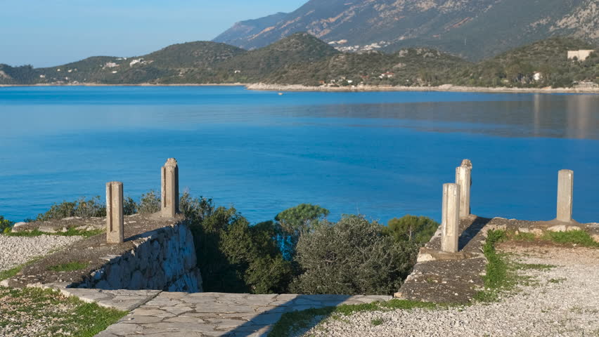 Tourist walking towards beautiful blue sea view. Senior traveler carrying backpack descending stone stairway, revealing breathtaking mediterranean seascape with azure waters, mountainous horizon