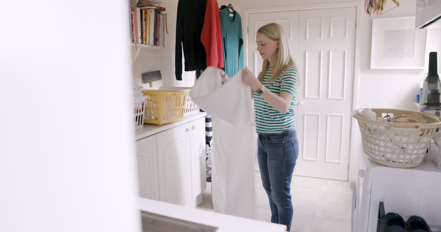 Home, laundry and woman fold fabric or fresh sheets and putting in laundry basket. Hygiene, housework and young female organizing bed linen after cleaning and washing in laundry room of house alone.
