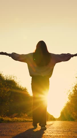 Meditation outdoors healthy lifestyle. Girl walking on asphalt road towards sun raising her hands. Women travel in fresh air. Woman walking on road at sunset. Tourist going on adventure trip, vacation