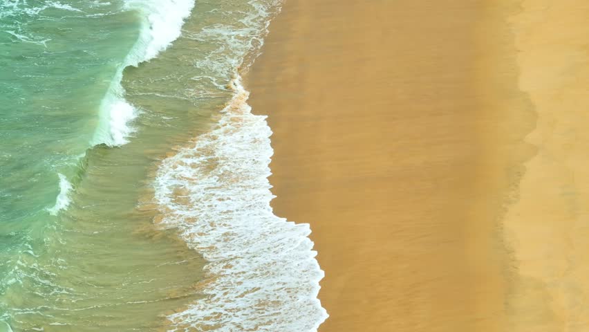 An aerial view offers a stunning view of the coastline, where the waves gently crash onto the beach. The vibrant turquoise water and soft golden sand create a harmonious scene of natural beauty.
