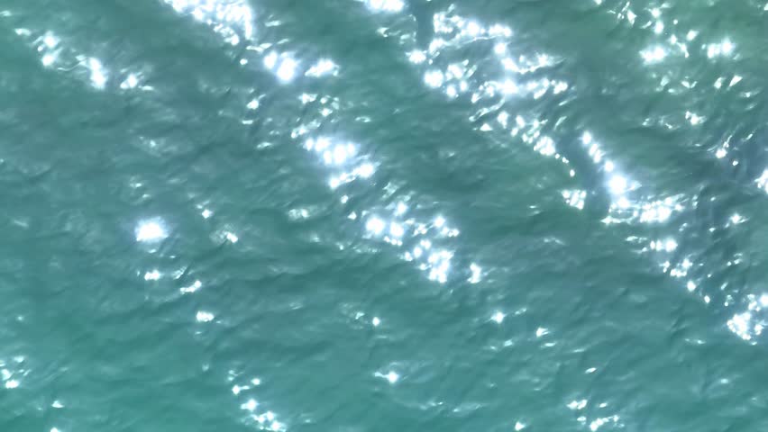 The aerial view captures the serene beauty of the ocean's surface, with sunlight reflecting off the shimmering water, creating a peaceful, soothing scene of natural light and movement.

