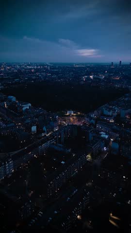 Vertical aerial of lights coming on in building as night falls over Copenhagen suburb