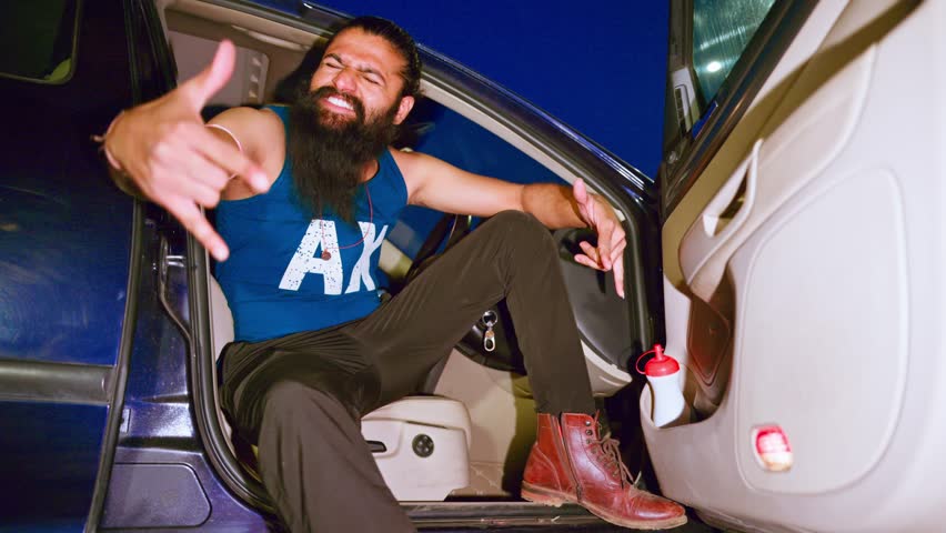 Bearded hip hop star dances in an unlatched car, Rap artist gesturing with hands while dancing, Freestyle Urban dancer moves on music video boldly, Passionate guy enjoying song seated at the front
